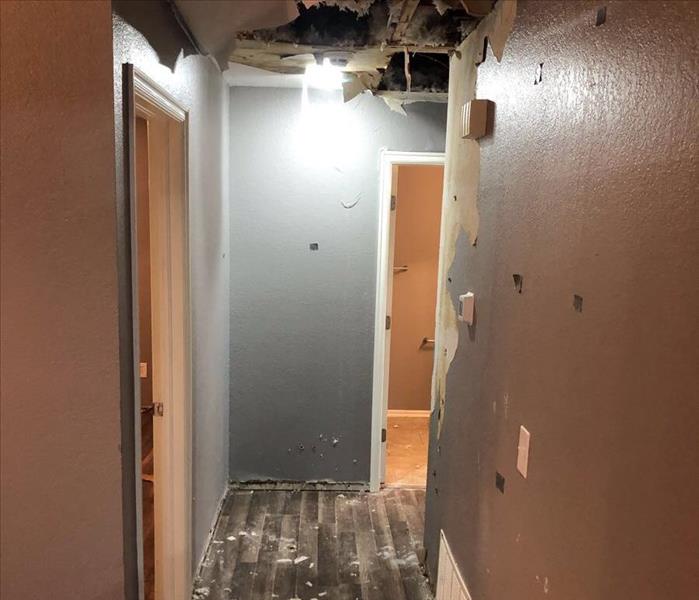 A hallway with a hole in the ceiling that has left sheetrock and insulation littering the floor