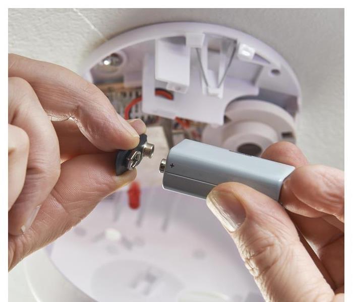 The hand of someone changing the battery of a smoke detector